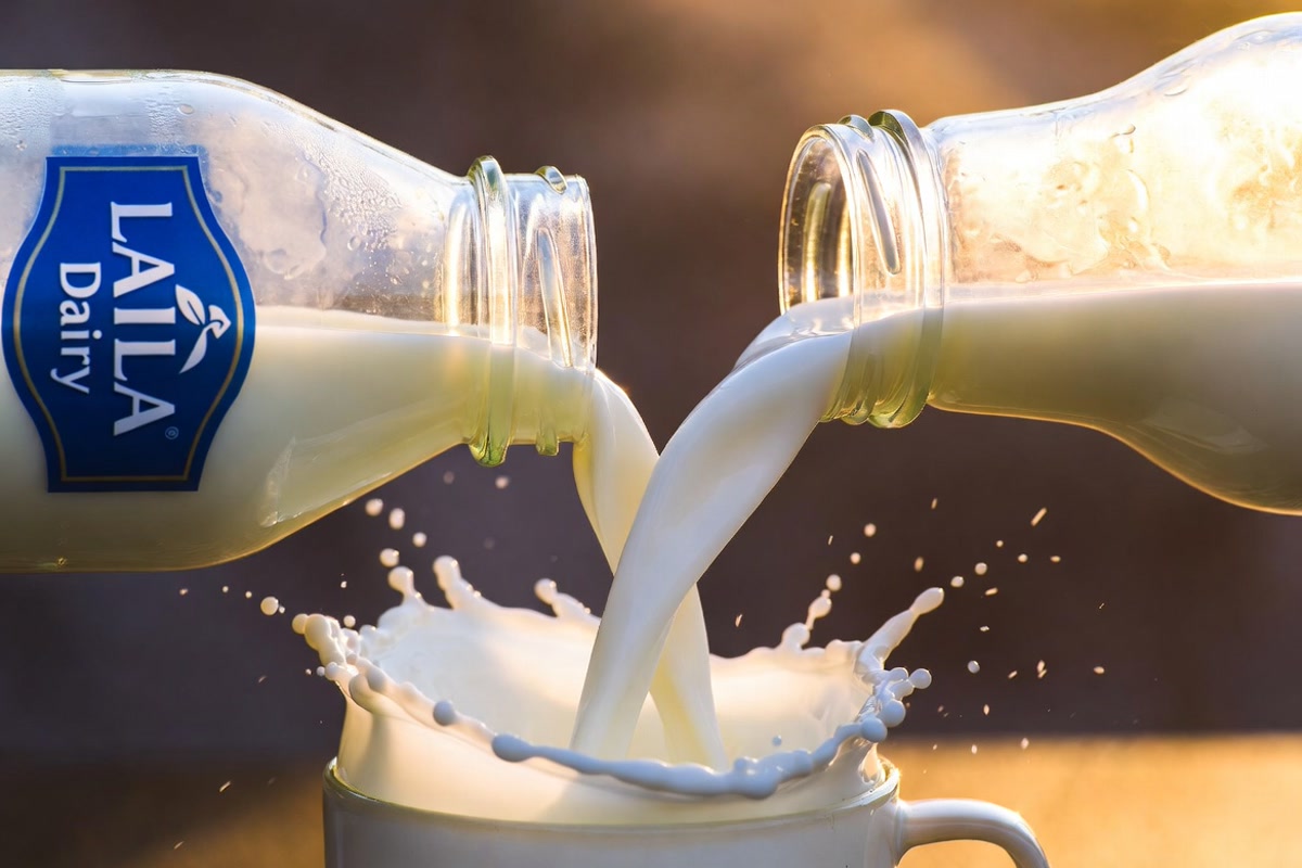 Close-up of fresh milk being poured from a glass bottle into a ceramic cup at golden hour